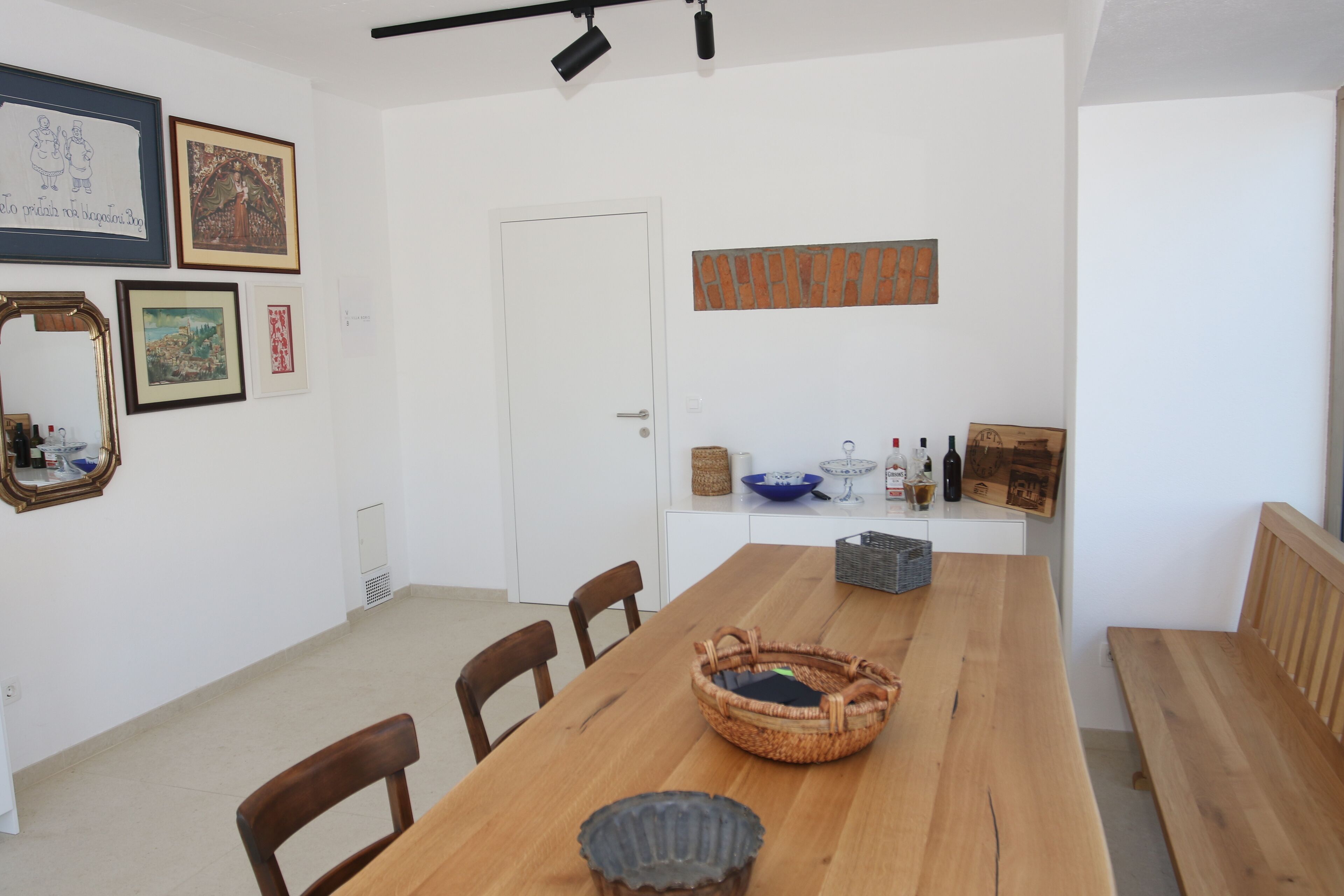 A dining area with a wooden table, chairs, a bench, and a wall adorned with framed artwork.