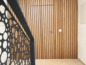 A wooden door with a keyhole and a light switch, a black metal railing with circular cutouts, and a beige floor. - Villa Boris (Starše)
