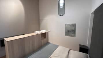 A modern bedroom with a wooden bed, a bedside table with towels, a hanging light fixture, and a wall-mounted artwork.