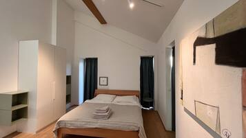 A modern bedroom with a wooden bed, a wardrobe, a small seating area, and a painting on the wall.