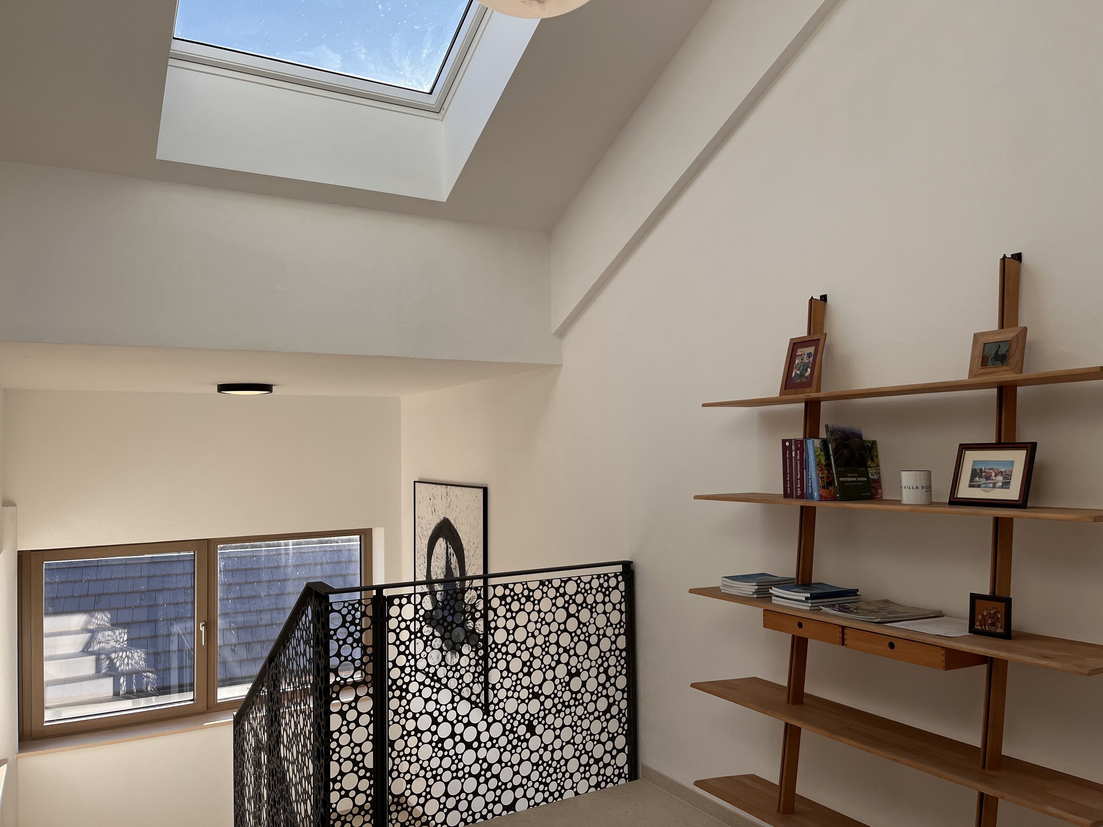 Una habitación con tragaluz, una escalera y una estantería con libros y cuadros.