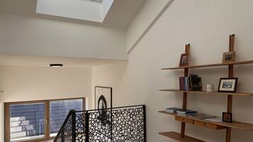 Una habitación con tragaluz, una escalera y una estantería con libros y cuadros.