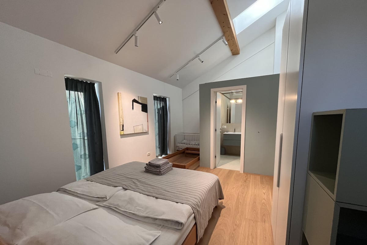 A modern bedroom with a large bed, a walk-in closet, and a bathroom visible through an open door.