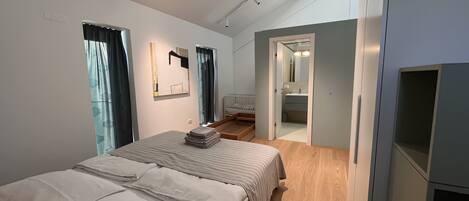 Quarto moderno com uma cama grande, um closet espaçoso e um banheiro visível por uma porta aberta.