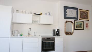 Een moderne keuken met witte kastjes, een koffiezetapparaat en een oven. Er hangen kunstwerken in lijsten aan de muur.