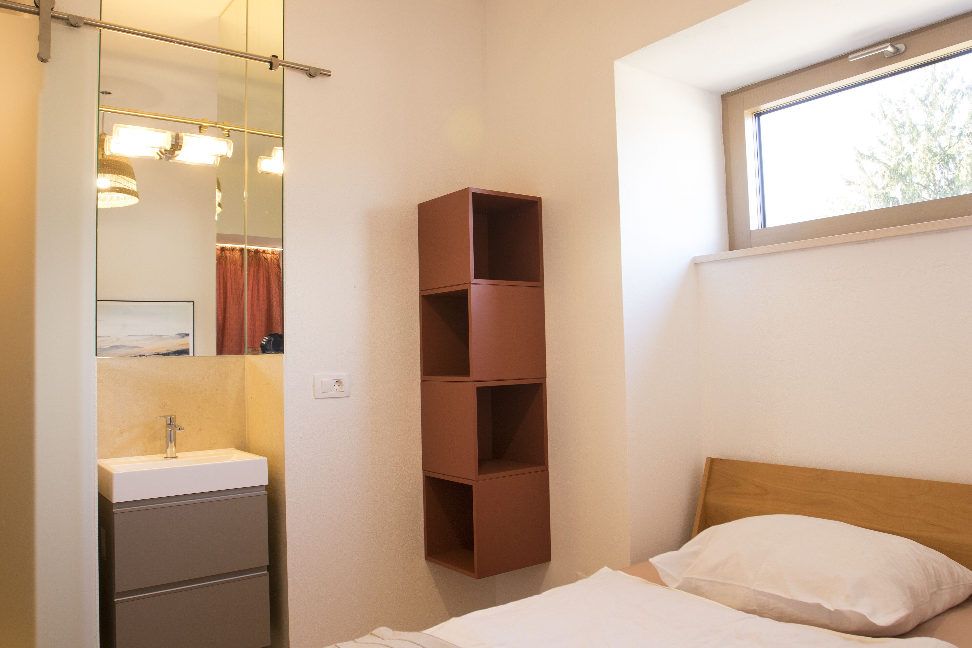 Un dormitorio con cama, cabecera de madera, ventana y estante marrón.