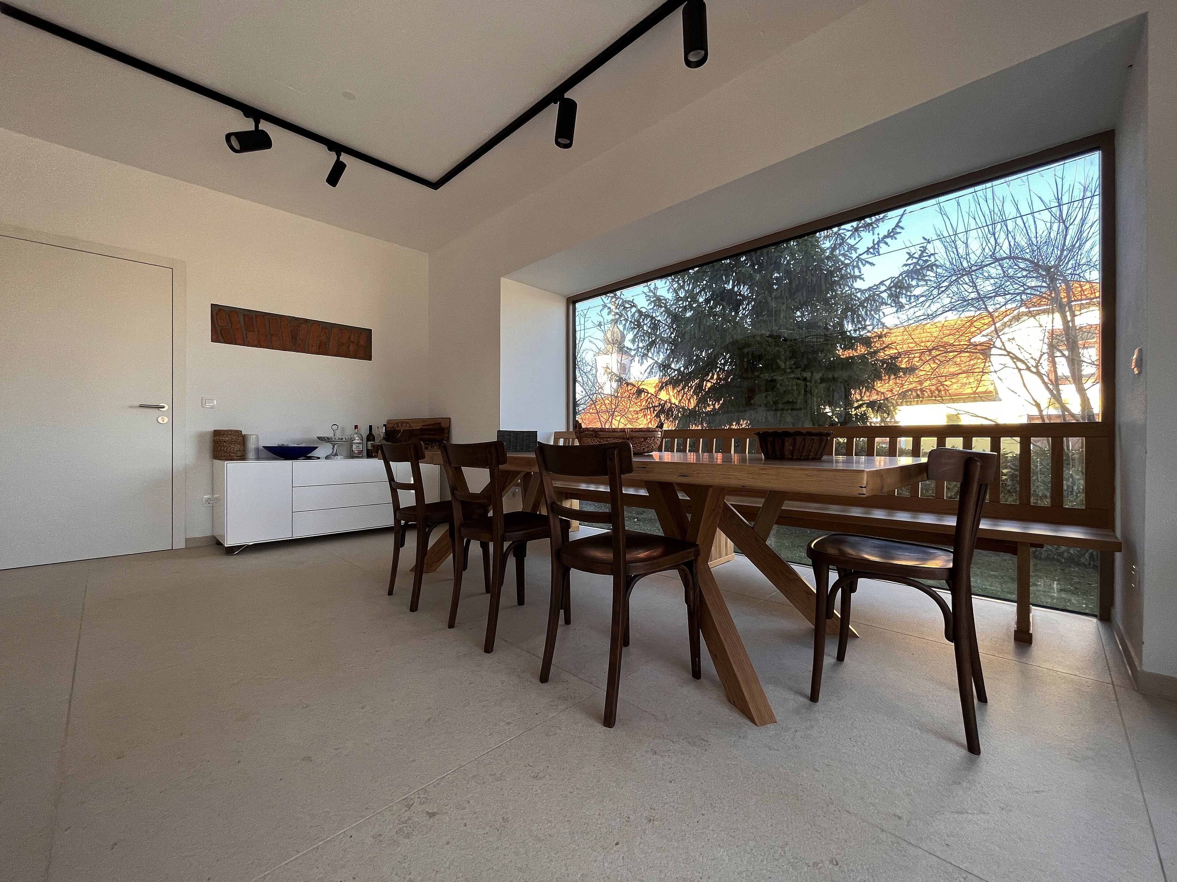 A modern dining area with a large window, a wooden table, and chairs.