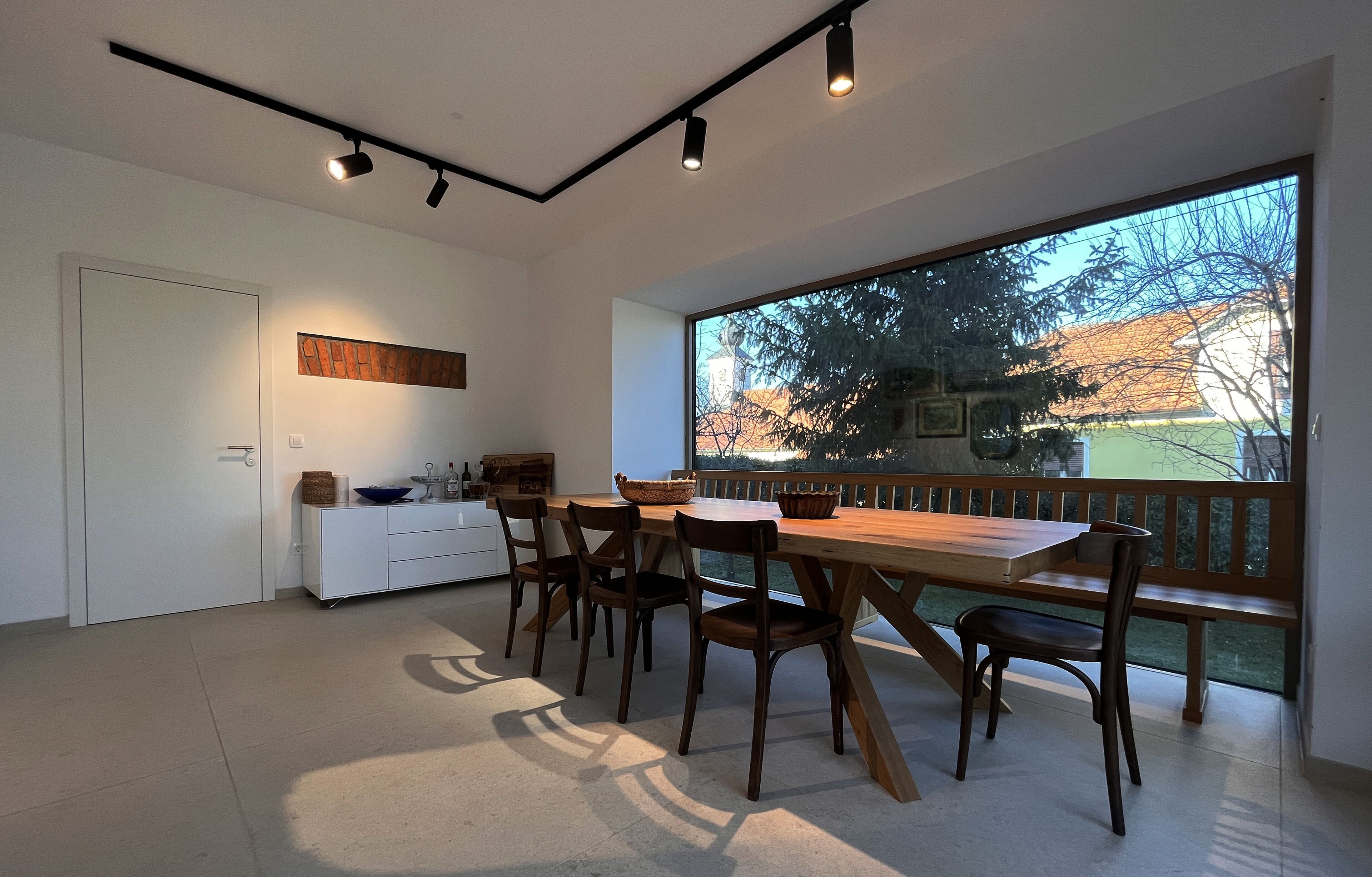 Una cocina moderna con un ventanal grande, un área de comedor con mobiliario de madera y vistas a un balcón con barandilla.