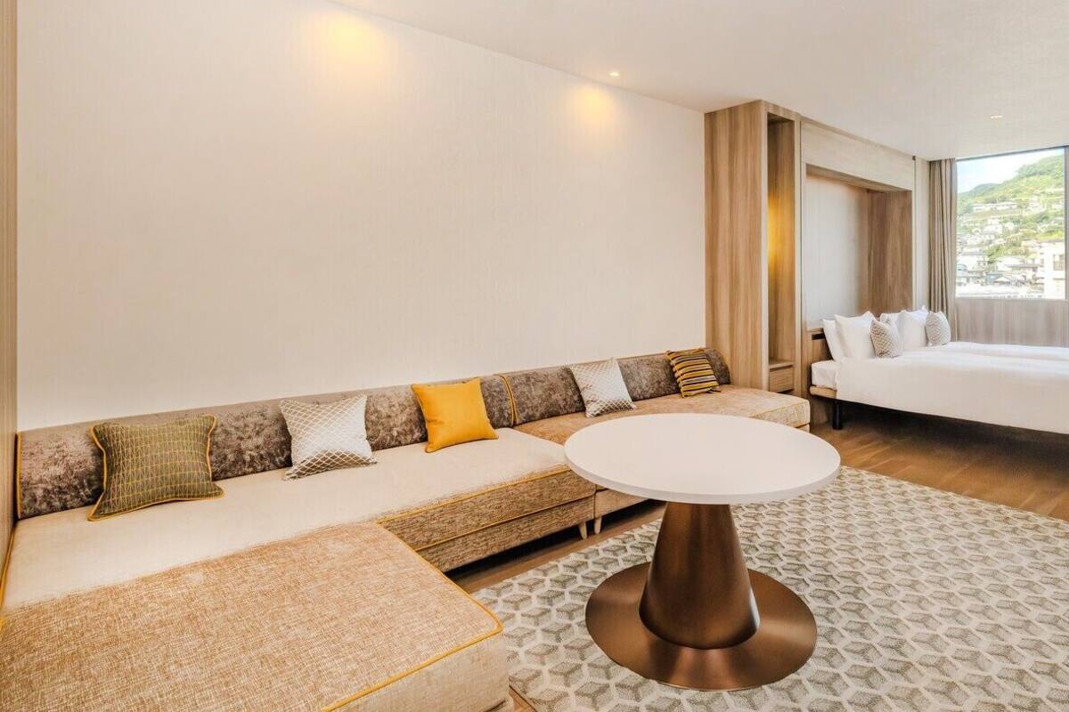 Una camera d'albergo con un divano, un tavolino rotondo, un letto e una grande finestra.