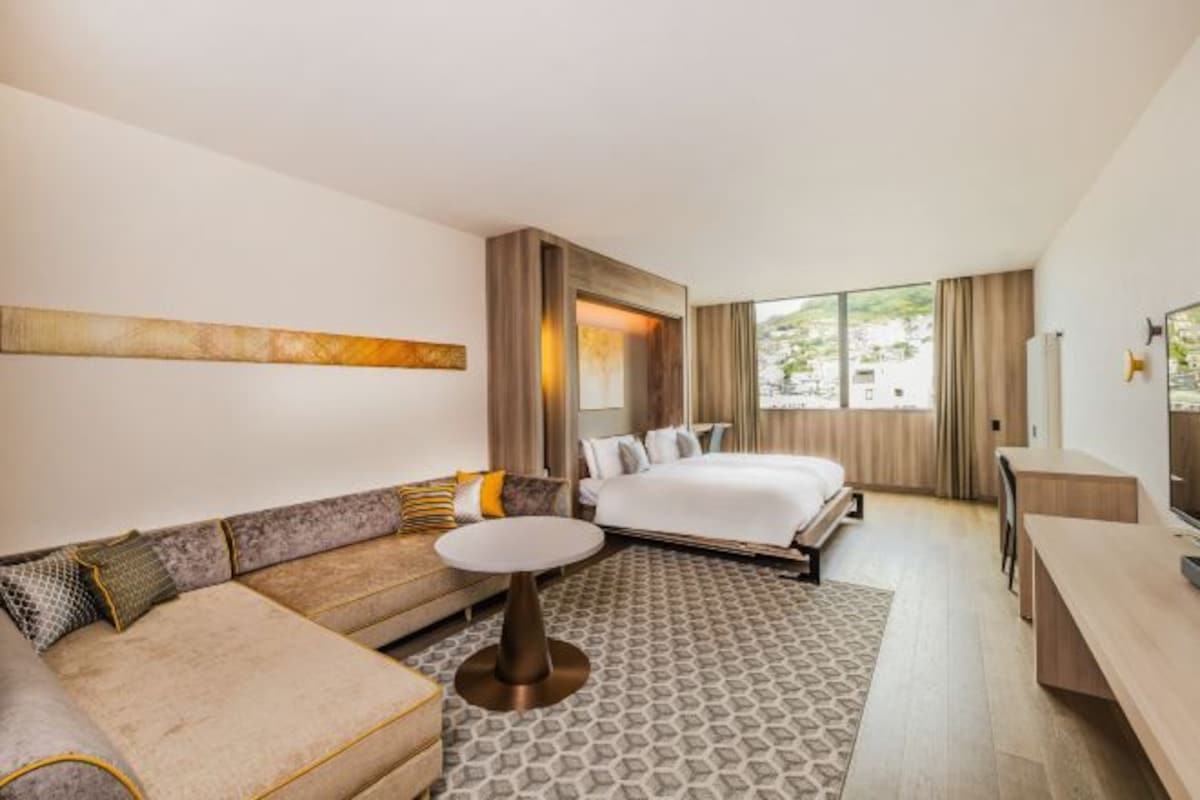 A modern hotel room with a large bed, a sofa, a small table, and a TV.