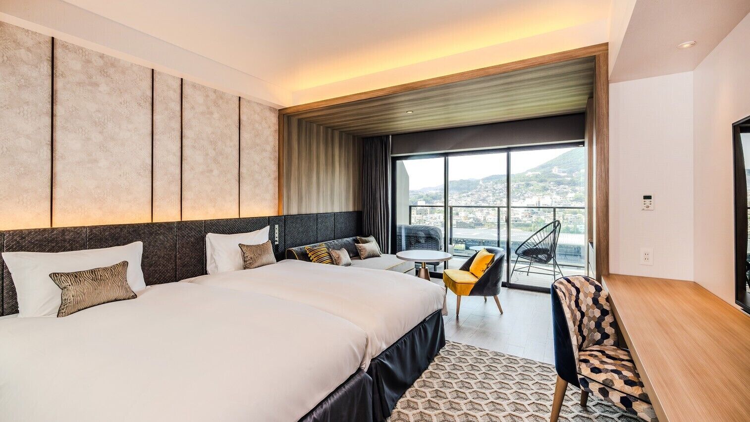 A hotel room with a large bed, a small table, two chairs, and a view of the city.
