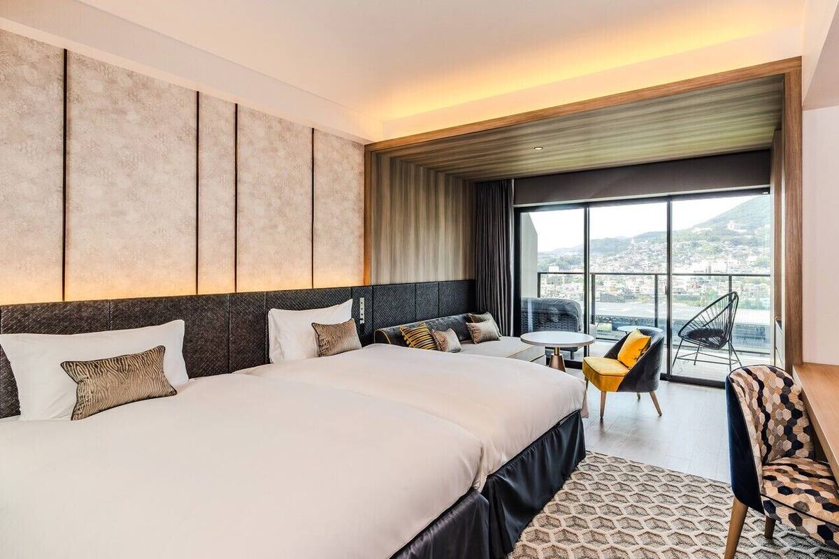 Camera d'albergo con un letto grande, un tavolino, due sedie e vista sulla città.