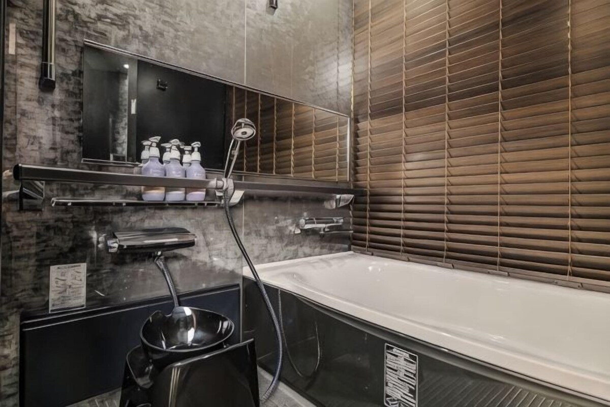 A bathroom with a bathtub, a mirror, a shelf with toiletries, and a showerhead.