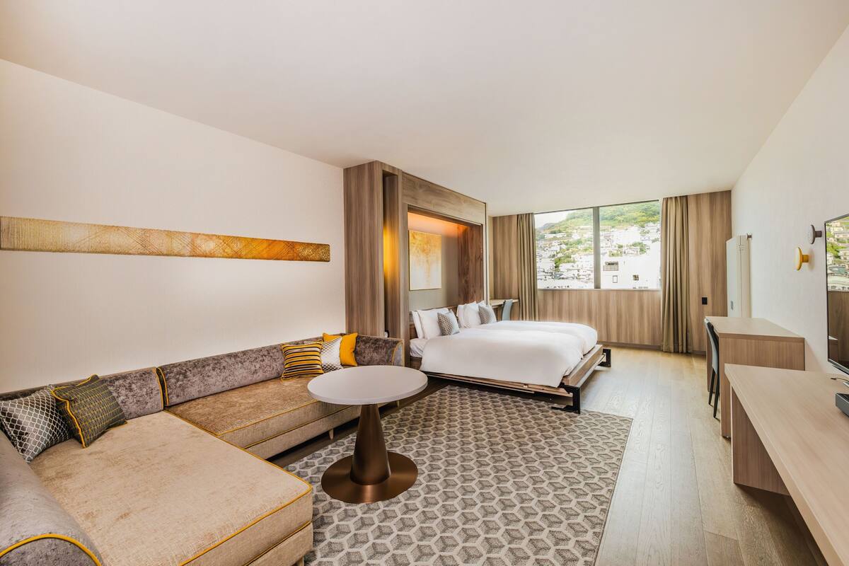 Camera d'albergo moderna con divano, un letto, un piccolo tavolo rotondo, una televisione e un'ampia finestra con vista sulla città.
