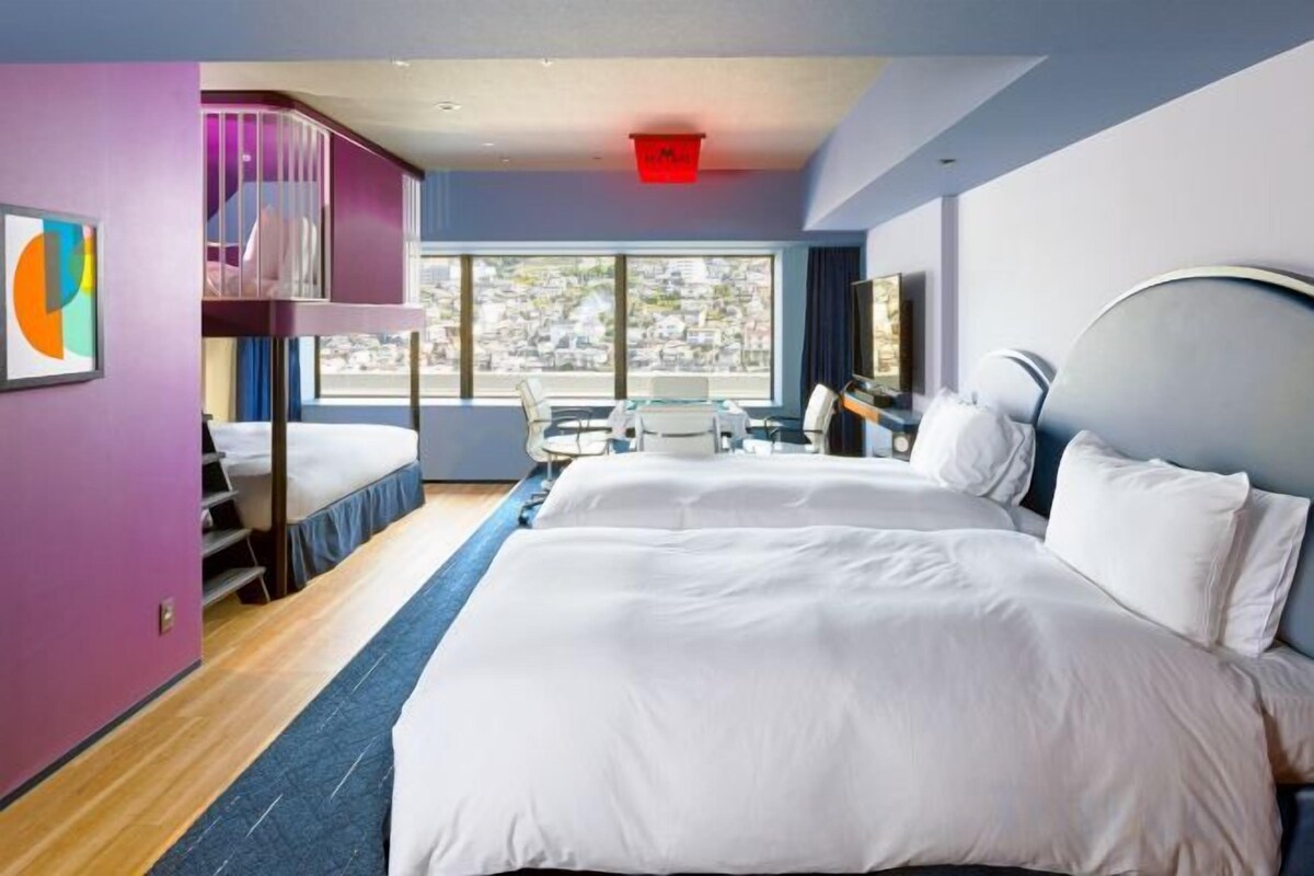 Una habitación de hotel con literas, un escritorio y un ventanal grande.