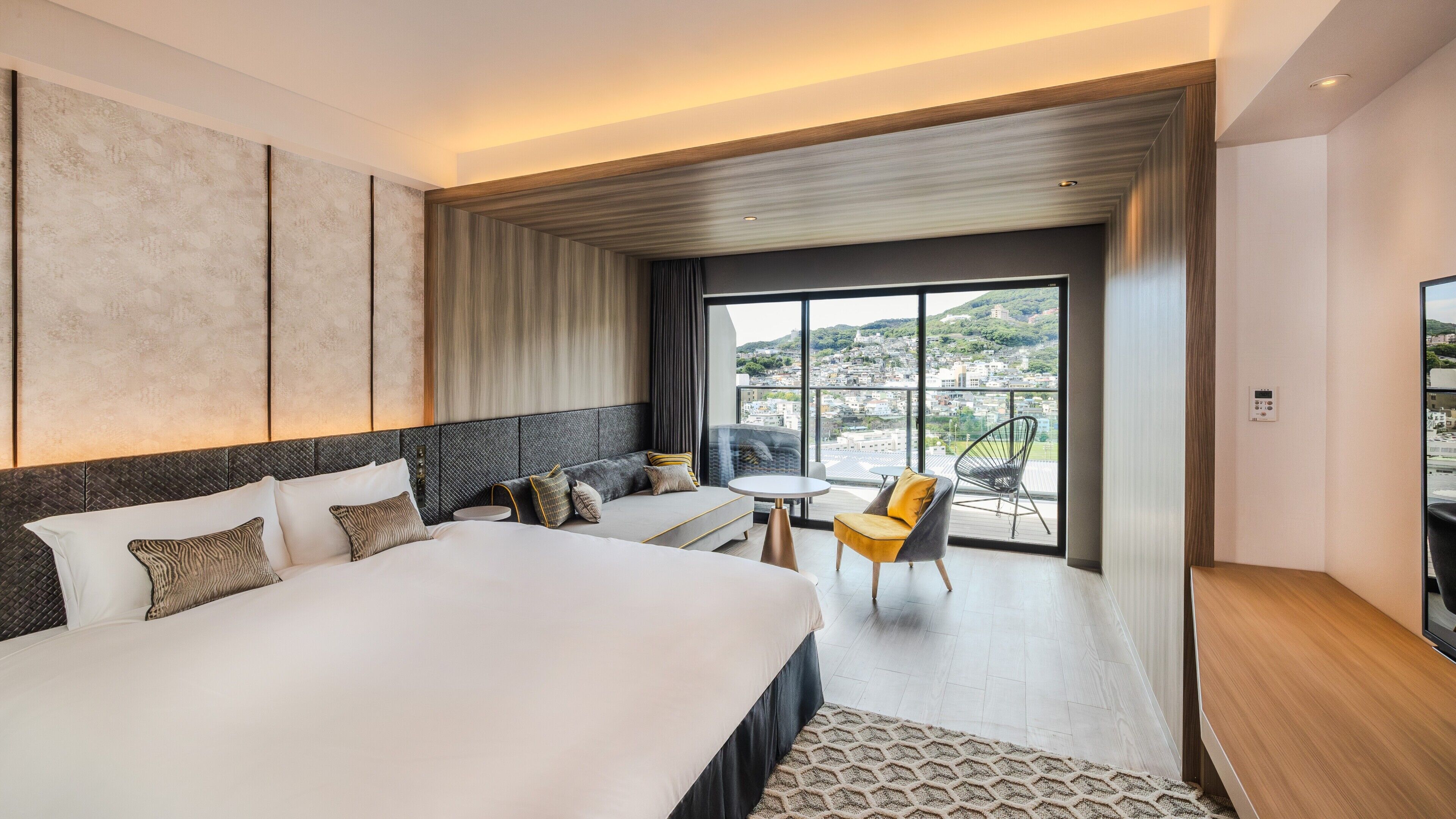 Et moderne hotelværelse med en stor seng, en sofa, et lille bord og en stol. Der er et stort vindue med udsigt over byen.
