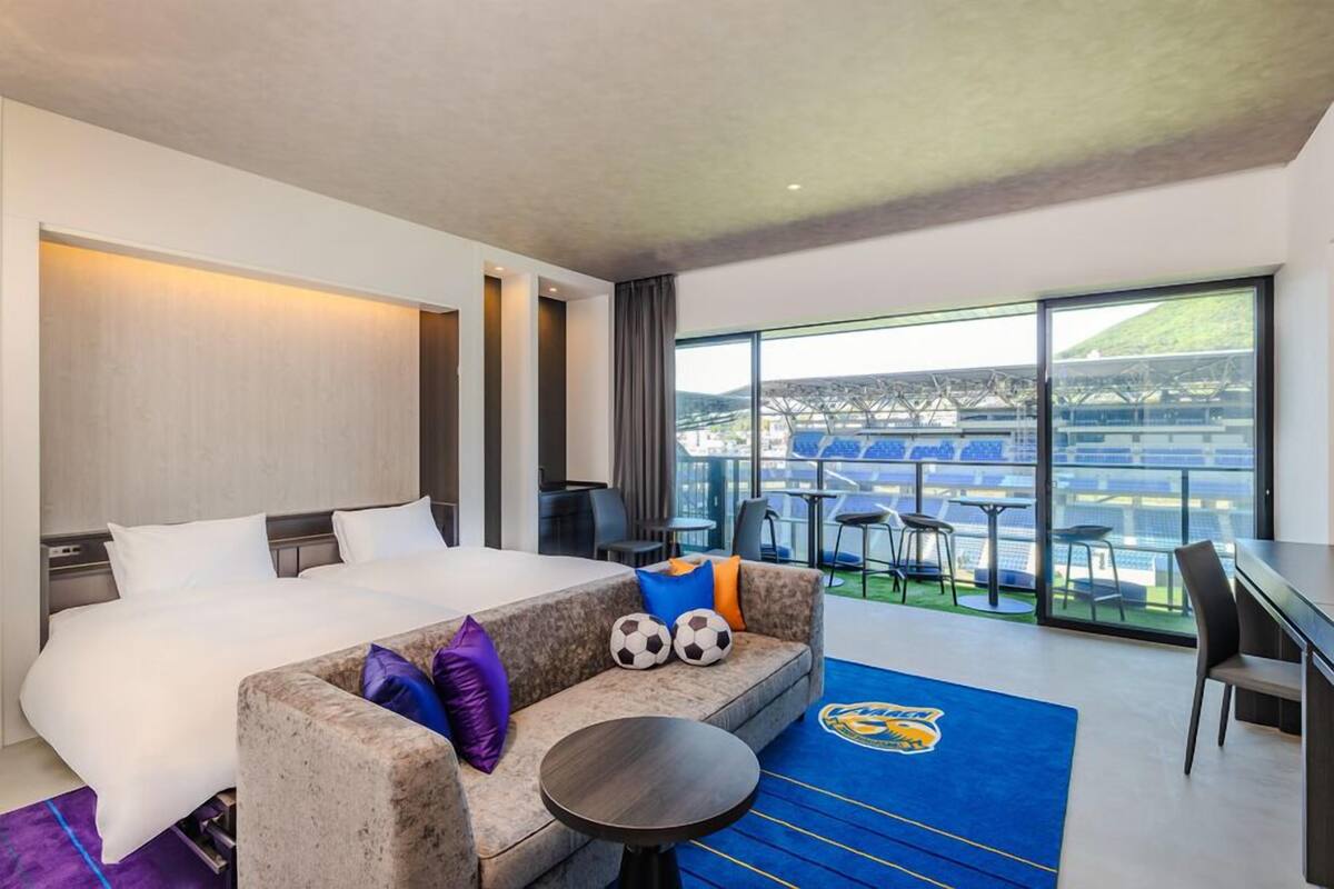 Camera d'albergo con letto, divano, tavolo da pranzo e un'ampia finestra vista stadio.
