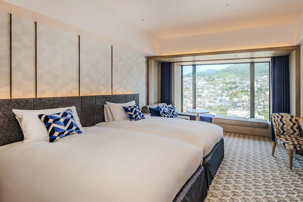 Una camera d'albergo con un letto grande, una scrivania, una sedia e un'ampia finestra vista città.