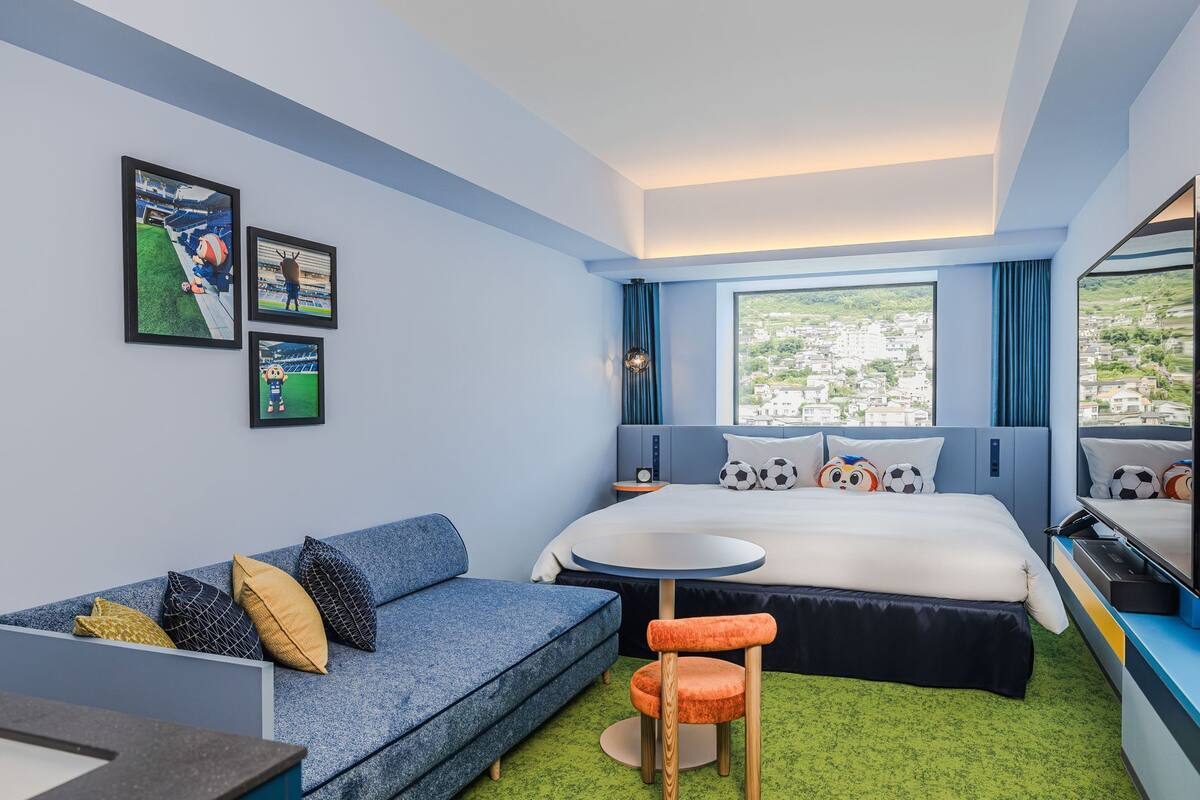 Una camera d'albergo con un letto, un divano, un tavolino, una TV e quadri appesi alle pareti.