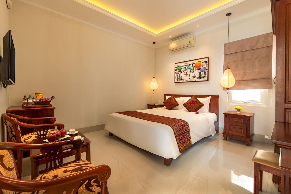Une chambre d’hôtel avec un grand lit, des meubles en bois, une petite table avec un vase et un tableau au mur.
