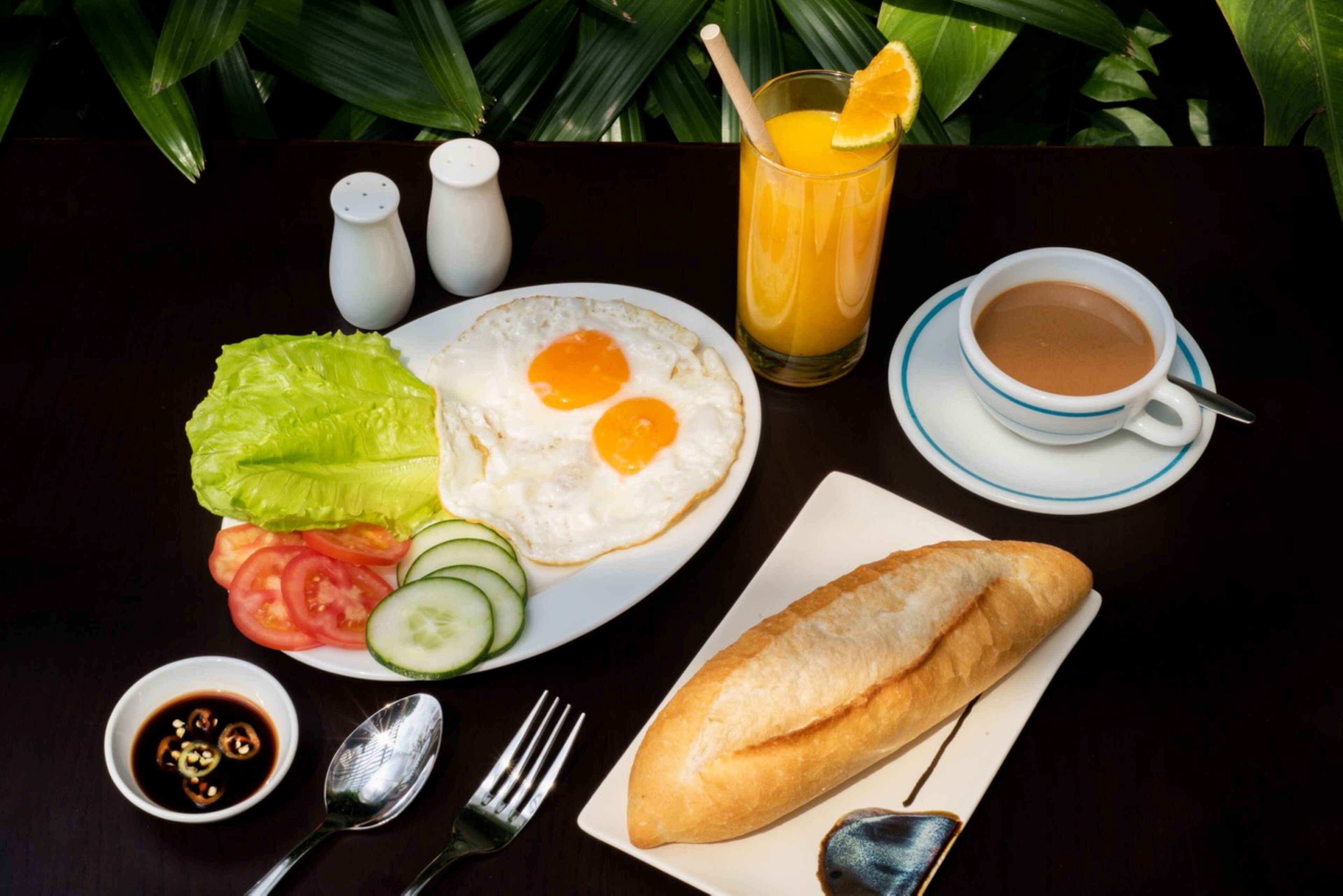Une assiette de petit-déjeuner comprenant des œufs, des légumes, un petit pain, une tasse de café et un verre de jus d’orange.