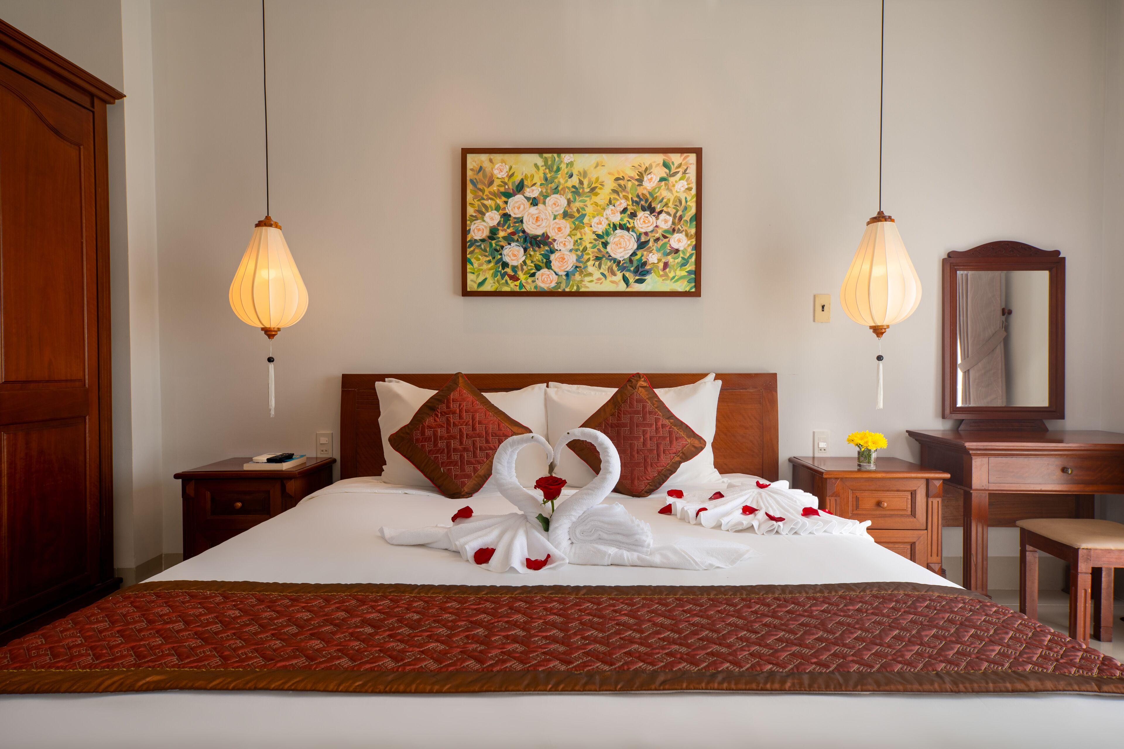 A hotel room with a neatly made bed, a wooden headboard, a painting on the wall, and a desk with a mirror.
