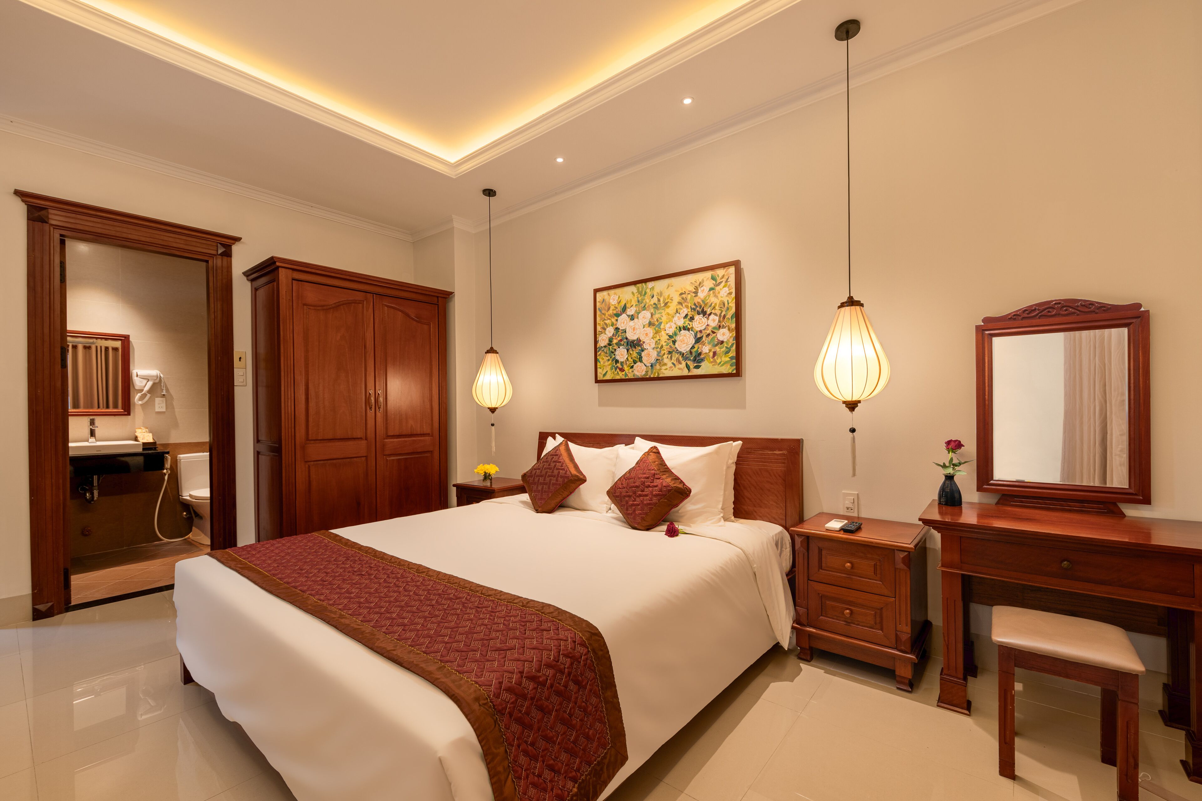A hotel room with a large bed, wooden wardrobe, bedside table with lamp, and a mirror.