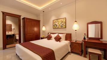 A hotel room with a large bed, wooden wardrobe, bedside table with lamp, and a mirror.