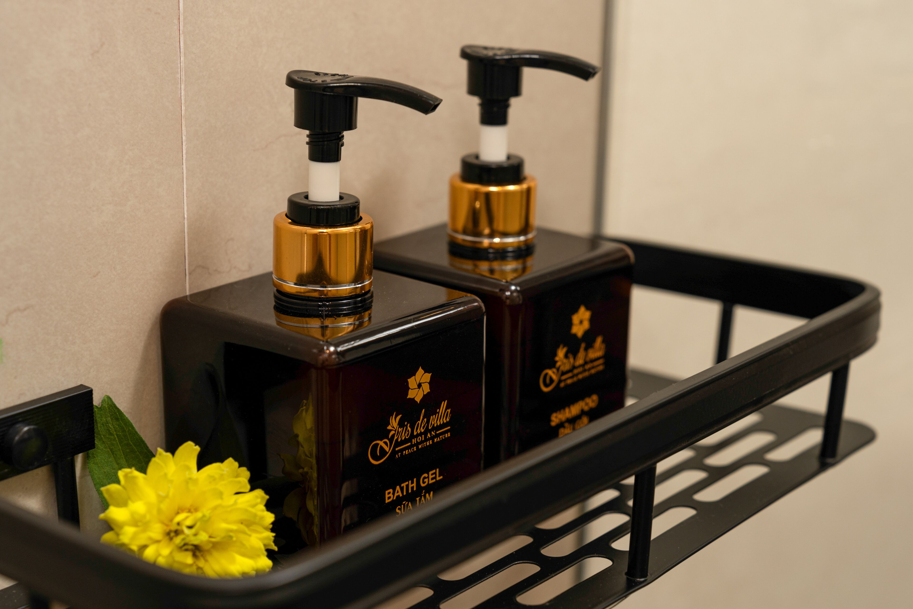 Two bottles of bath gel and a yellow flower on a black shelf.