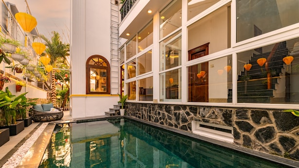 A pool area with stone walls, a staircase, and potted plants. - Iris De Villa Hoi An (Da Nang)