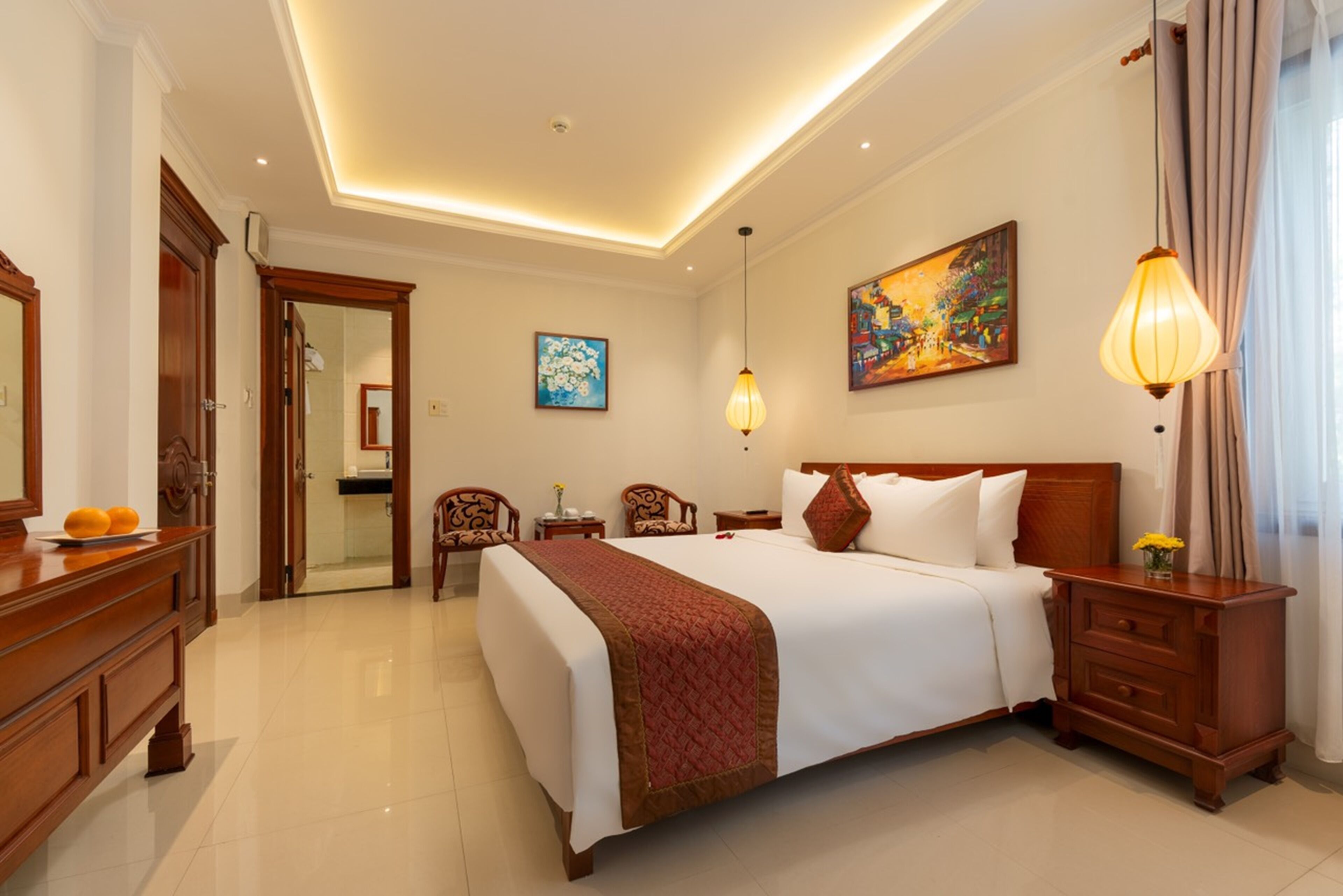 A hotel room with a large bed, wooden furniture, a painting on the wall, and a ceiling light.