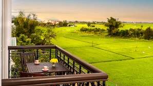 A balcony with a table, chairs, and a view of a green field. - Iris De Villa Hoi An (Da Nang)