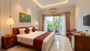A hotel room with a large bed, a desk, a television, and a view of the outdoors. - Iris De Villa Hoi An (Da Nang)