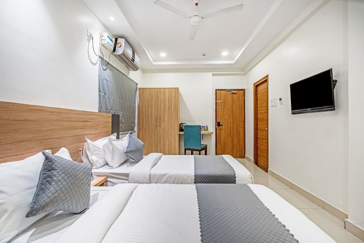 Ein Hotelzimmer mit zwei Betten, einem Schreibtisch, einem Stuhl, einem Fernseher und einem Deckenventilator.