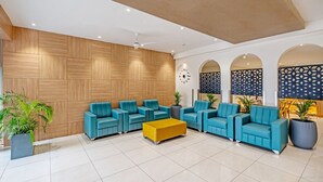 A modern lobby with wooden panel walls, blue sofas, a yellow ottoman, and potted plants. - SAPPHIRE BLISS HOTEL (Hyderabad)