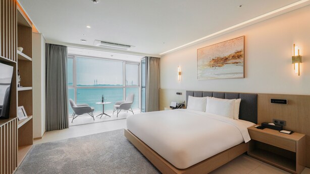 A modern hotel room with a large bed, bedside tables, a desk, and a view of the sea. - WAVE M HOTEL WEST (Siheung)