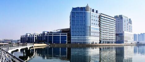 A modern hotel with a glass facade, located beside a calm body of water, reflecting the buildings.
