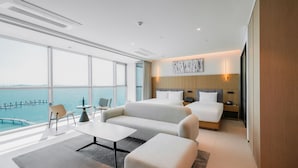 A modern hotel room with a large window overlooking a body of water, a bed, a sofa, a small table, and a chair. - WAVE M HOTEL WEST (Siheung)