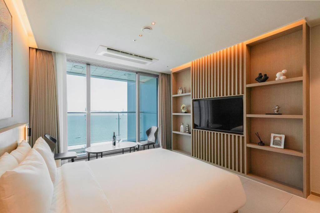 Quarto de hotel com cama, televisão, mesa pequena e varanda com vista.