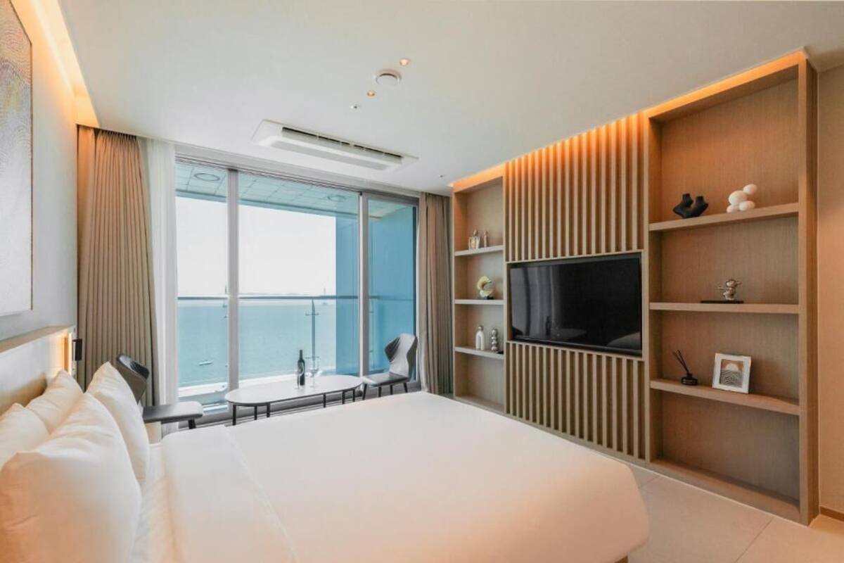 A hotel room with a bed, a TV, a small table, and a balcony with a view.