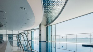 An indoor swimming pool with clear glass walls, a metal handrail, and a view of the sea. - WAVE M HOTEL WEST (Siheung)