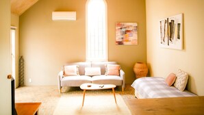 A cozy living room with a high ceiling, a large window, a sofa, a coffee table, and artwork on the walls.