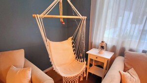Una sala de estar acogedora con dos sofás, un sillón colgante, una mesita y una ventana con cortinas de gasa.