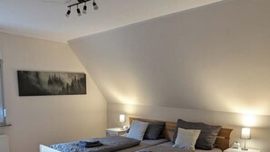 Un dormitorio con una cama de madera, dos mesitas de noche con lámparas, un cuadro en la pared y un techo inclinado.