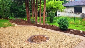 Un jardín ajardinado con un área circular de grava, árboles y un arbusto pequeño.