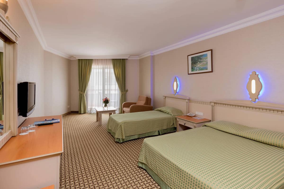 A hotel room with two beds, a desk, a chair, a TV, and a window with curtains.