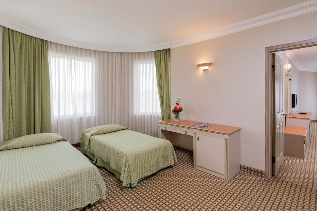 A hotel room with two beds, a desk, a mirror, and a small bathroom.