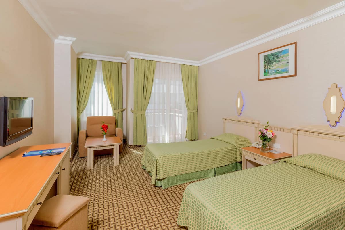 A hotel room with two beds, a desk, a chair, a TV, and a painting on the wall.
