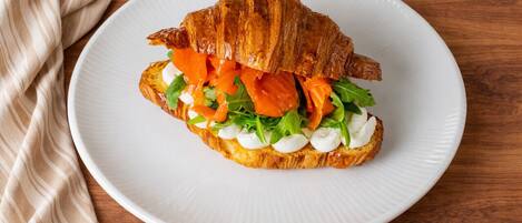 Sándwich de croissant con salmón ahumado, rúcula y queso crema sobre un plato blanco.