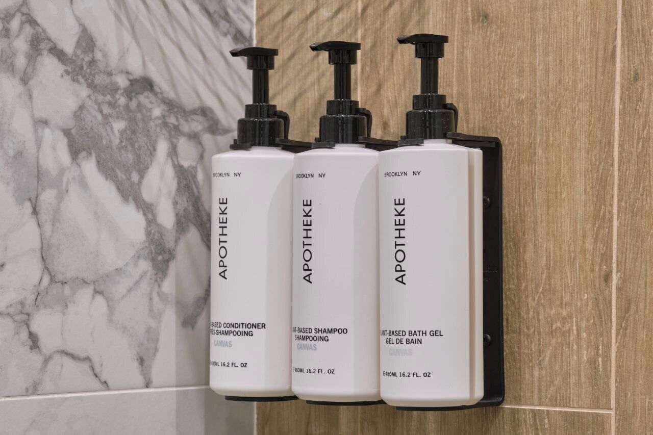 Three bottles of Apotheke products on a black shelf against a marble and wooden background.